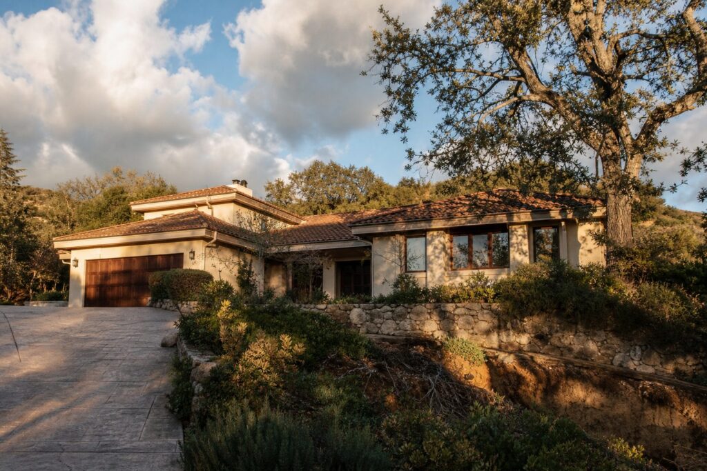 Mediterranean-style hillside home in Granada Hills with terracotta roof, stucco walls, and evidence of storm damage to landscaping and structures.
