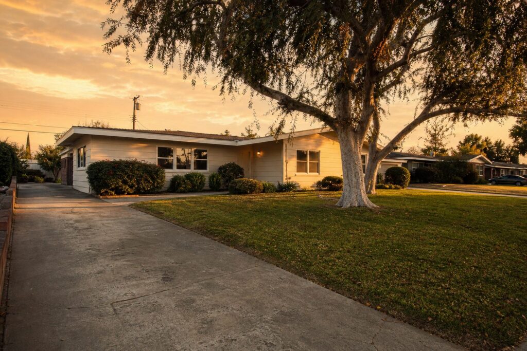 Warm-lit 1960s ranch home with pepper tree and established landscaping in Old Granada Hills at sunset.