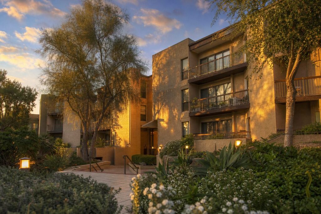 Mid-rise 1970s stucco condo building in Valencia with mature landscaping and entry courtyard at golden hour.