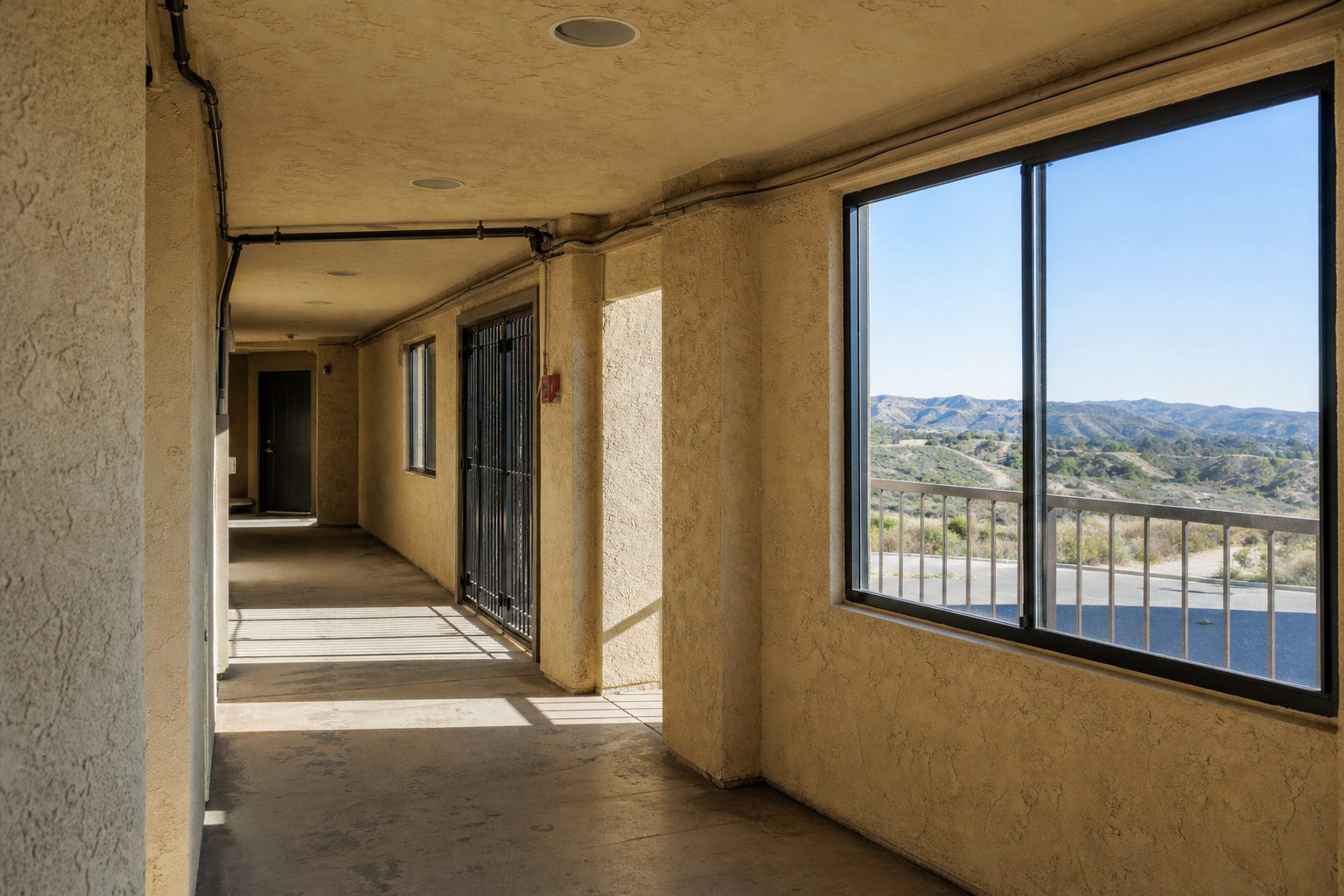 Interior hallway of 1980s Saugus condo with concrete flooring and window view toward Canyon Country landscape and distant hills.