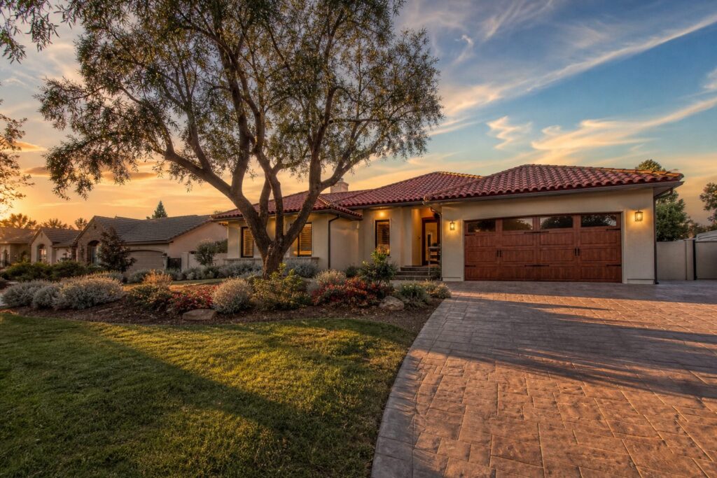 Single-story stucco home with red tile roof and mature pepper tree in residential Northridge neighborhood at golden hour.